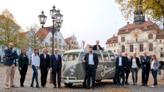 Teamfoto mit den Mitarbeitern von Sallier Immobilien auf dem Lüneburger Marktplat vor einem VW Bulli mit Sallier